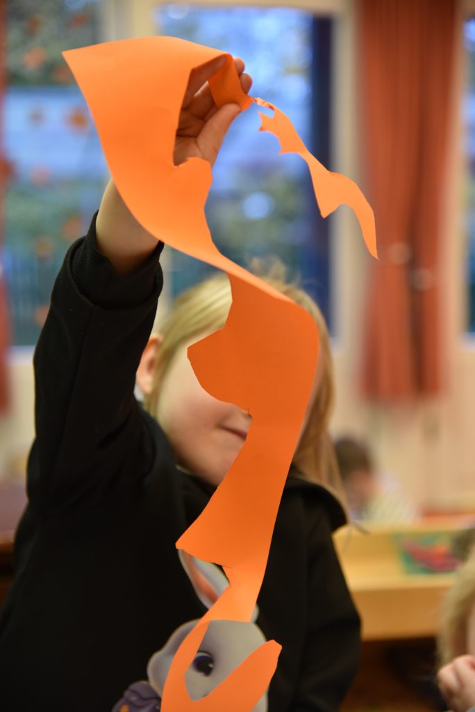 Kind hat einen orangen Papierbogen ausgeschnitten