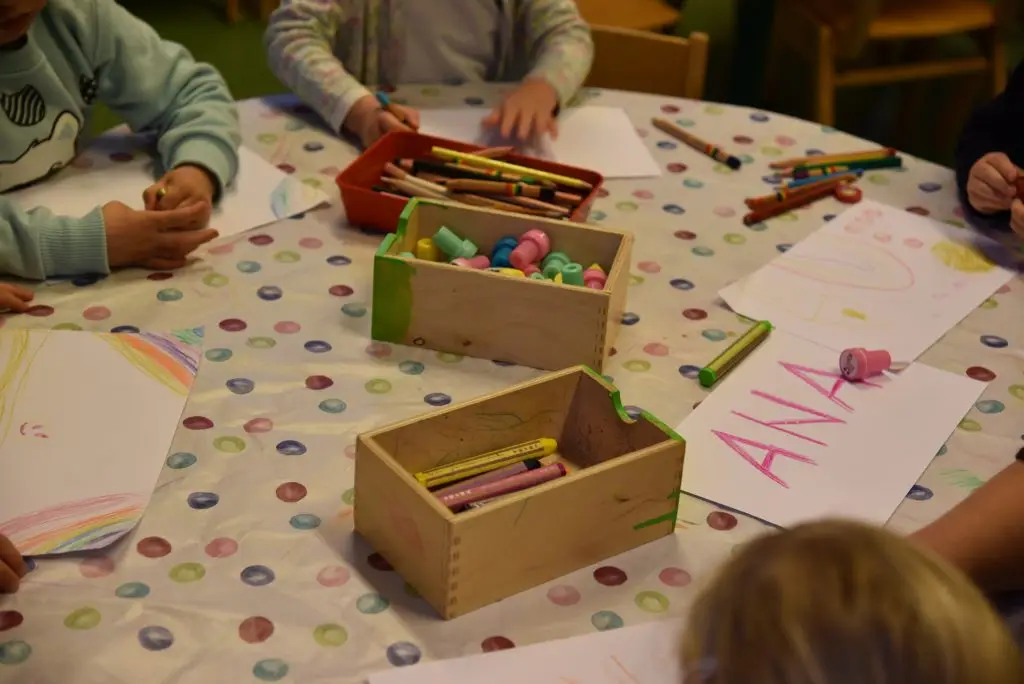 Kindergruppe sitzt an einem runden Tisch und malt mit Buntstiften