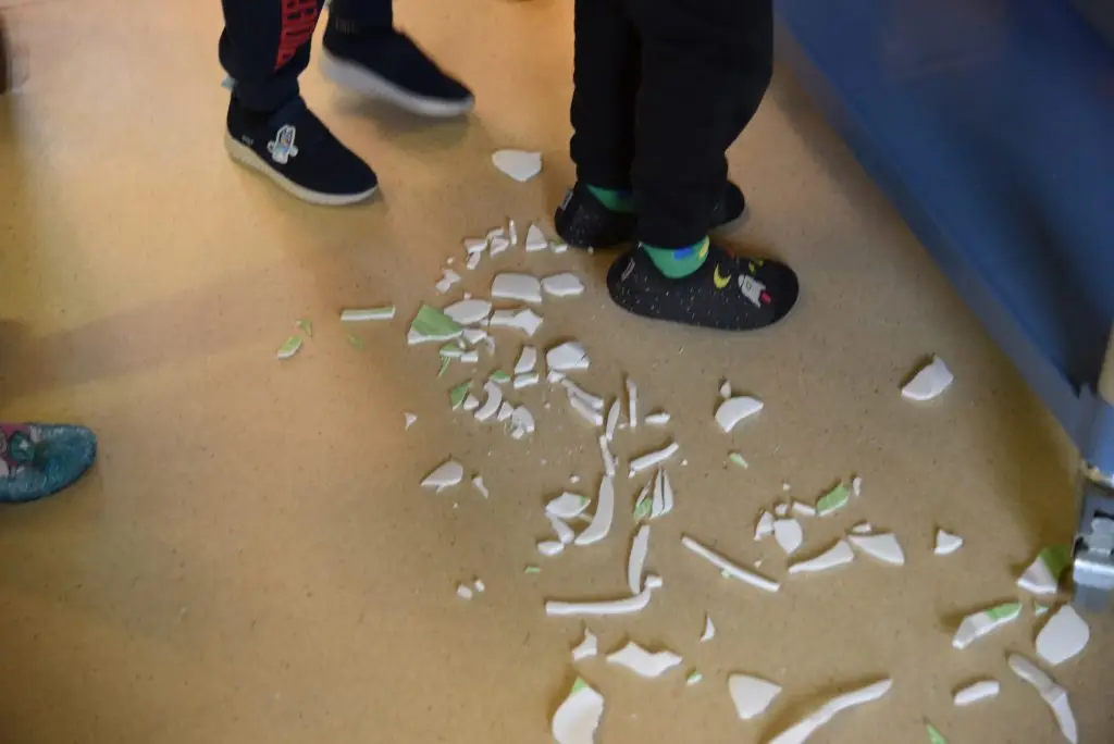 Kinder beim Zusammenstellen von Geschirr. Auf dem Boden liegen Porzellanscherben