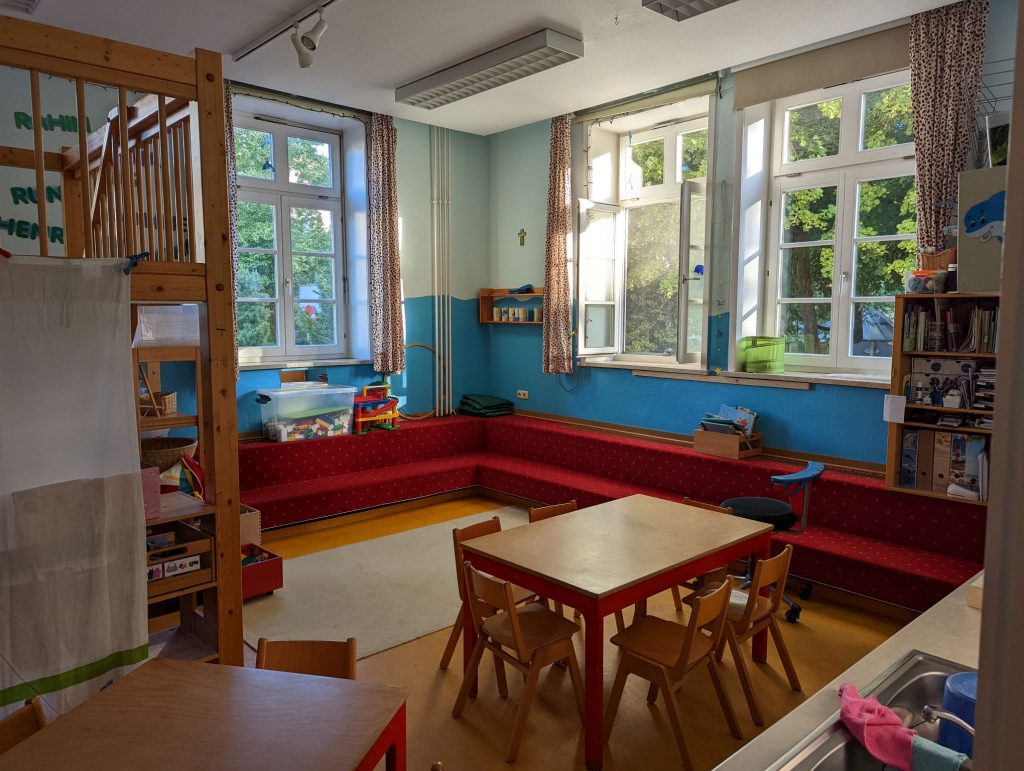 Gruppenraum mit Tisch und Stühlen und einer roten Sitzbank unter dem Fenster Kita St. Ludwig Celle